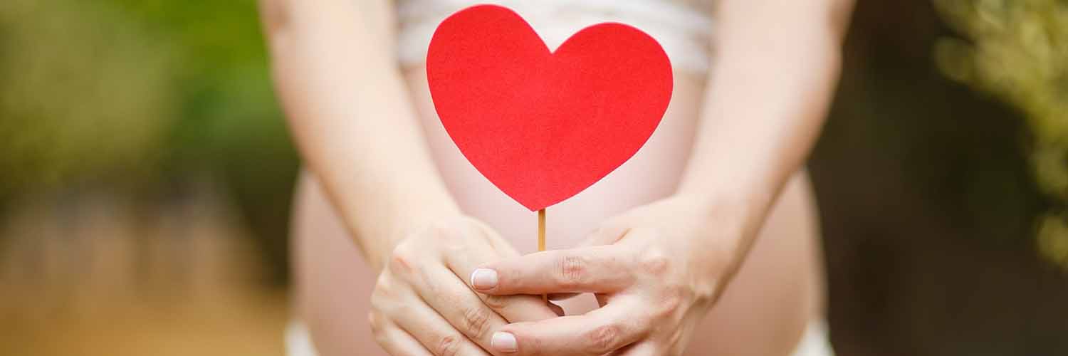 Mujer embarazada con corazón de cartón en color rojo apoyado sobre la barriga.